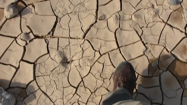 After a flood in the desert wadi on the road to Jebal Jais in Ras al Khaimah, United Arab Emirates, a person talks across the cracked, dry, clay showing the texture and design of the mud and no water.