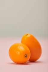 two ripe kumquats on pink surface on grey