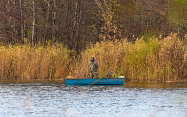 Fisherman catches from a boat on the pond in autumn