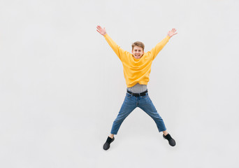 Fototapeta na wymiar Happy guy in Casual clothes jumps against the background of a white wall, street portrait. Young man is leap on the background of a white wall,jumping on the street, isolated. Copyspace