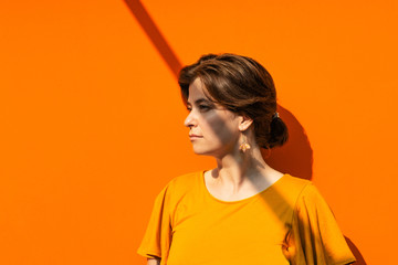 Beautiful young woman portrait in yellow blouse with linear shadow on her face and body. Orange...