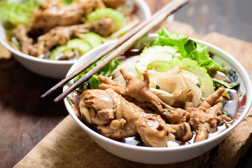 Rice noodles soup with stewed chicken wing and feet in a bowl with chopsticks