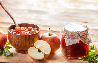 Wooden bowl and glass jar with apple jam and apples and green mint on wooden background. 