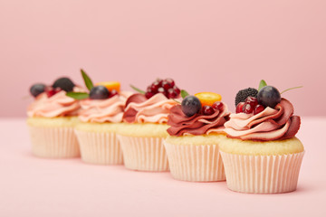 sweet cupcakes with fruits and berries on pink surface
