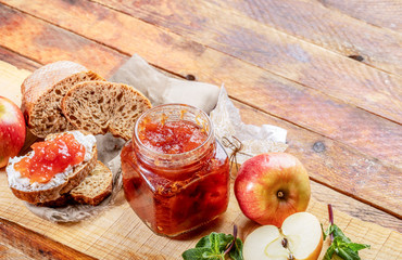 Open glass jar with apple jam, bread, smeared with curd and apple jam, and apples and green mint on...