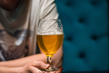 man's hand holds a glass of beer in bar