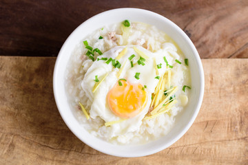 Thai rice soup or soft-boiled rice with pork and egg in the bowl on wooden background