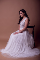 Fototapeta premium Beautiful young girl in a flying white dress. Flowing fabric. bride in white dress on beige background. gorgeous brunette on a studio background. Isolate