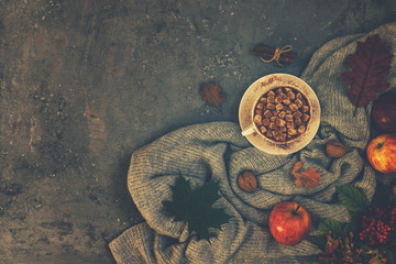 Autumn composition. Cup of coffee, blanket, autumn leaves, cinnamon sticks on brown background. Toned image. Top view, copy space.