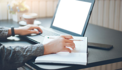 Closeup young asian woman working with laptop and writing on note