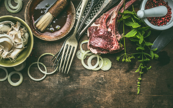 Grill Preparation With Racks Of Lamb With Fresh Seasoning, BBQ Simple Marinade And Kitchen Utensils On Rustic Wooden Background. Copy Space.