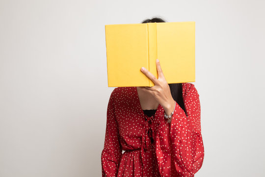 Young Asian woman with a book cover her face.