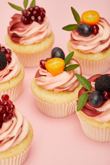 sweet cupcakes with fruits and berries on pink surface