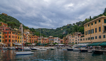 Fototapeta na wymiar Panoramic view to Portofino in Liguria coast. Province of Genoa, Italy. Sunny summer day panorama and blue dramatic sky with clouds. Ancient european italian terracotta color houses.