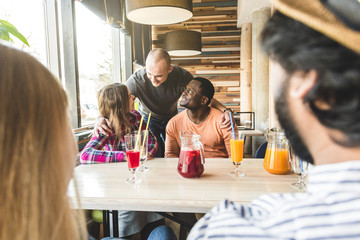 a group of young cheerful friends are sitting in a cafe, eating, drinking drinks, take selfies and take pictures. meeting, handshake and hugs