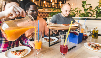 A company of multicultural  young people in a cafe eating pizza, drinking cocktails, having fun