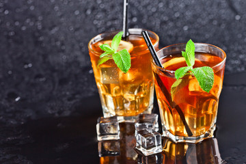 Two glasses with cold traditional iced tea with lemon, mint leaves and ice cubes.
