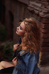 Obraz premium Stylish handsome curly blonde wearing chic little black dress and jeans jacket. Glamour girl posing and smiling at camera.