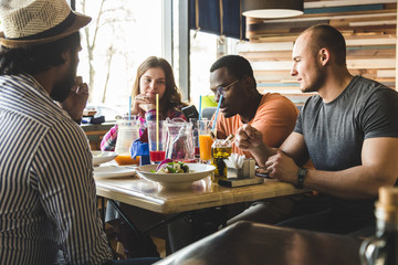 A company of multicultural  young people in a cafe eating pizza, drinking cocktails, having fun