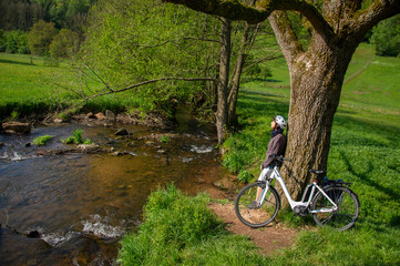 Fototapeta na wymiar Ausflug mit Elektro Fahrrad, Radfahrerin mach Pause an schöner Bachlandschaft