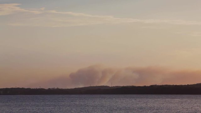 Bushfire season. Large plumes of smoke from a large bushfire or wildfire near a body of water. Best footage for emergency services and summer warnings to evacuate, a call to action of the firefighters