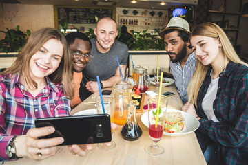 Group of young cheerful friends are sitting in a cafe, eating, drinking drinks. Friends take selfies and take pictures.