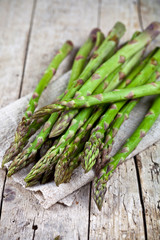 Bunch of fresh raw garden asparagus closeup and linen napkin on rustic wooden table background.