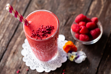 Delicious smoothie made of berries served on the table in glass with two straws in purple-red and white color combination