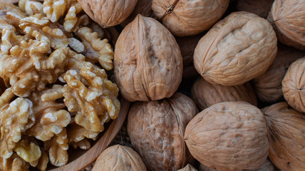 Walnuts in wooden round bowl, and walnuts with shell on sack surface