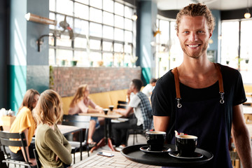 Portrait Of Waiter Serving Customers In Busy Coffee Shop