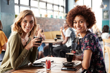 Portrait Of Two Female Friends Meeting Sitting At Table In Coffee Shop