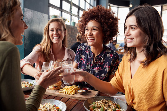 Four Young Female Friends Meeting For Drinks And Food Making A Toast In Restaurant