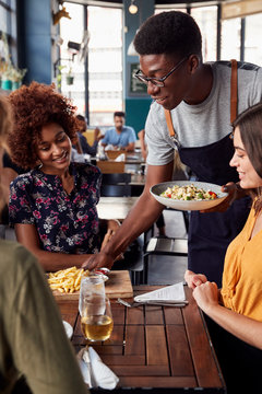 Waiter Serving Group Of Female Friends Meeting For Drinks And Food In Restaurant