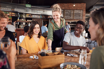 Waitress Serving Group Of Young Friends Meeting For Drinks And Food In Restaurant