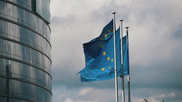 Three European Union flags flying at EC building on cloudy weather in slo-mo 