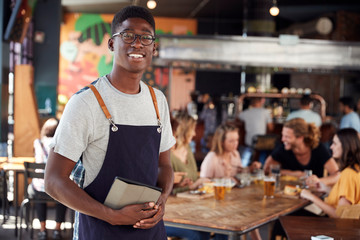 Portrait Of Waiter Serving In Busy Bar Restaurant