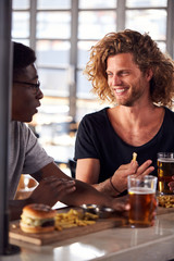 Two Male Friends Eating Food And Drinking Beer In Sports Bar