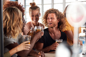 Group Of Male And Female Friends Celebrating Whilst Watching Game On Screen In Sports Bar