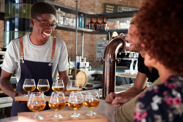 Waiter Serving Group Of Friends Beer Tasting In Bar