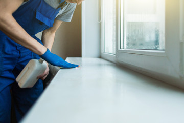 Close-up of a man in uniform and blue gloves washes a windows with window scraper. Professional home cleaning service