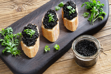 a glass jar of halibut caviar and baguette slices with the caviar and butter decorated with garden...