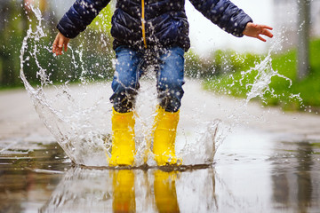 legs of child with yellow rubber boots jump in puddle on an autumn walk