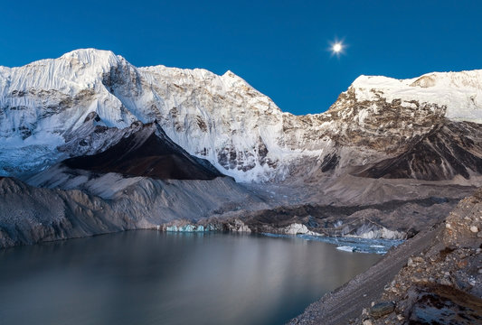 Gray moraine lake and snowy mountain peak in the moonlight in Himalayas, Nepal. Decent photo.