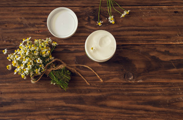 Obraz na płótnie Canvas Chamomile bouquet and fragrant body cream on a wooden table
