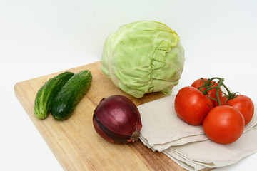 On a cutting board, tomatoes on a branch, cucumbers, a linen towel, cabbage, a head of red onions. Concept - vegetable diet, cooking soup.
