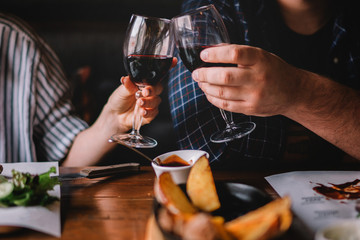 Glasses of red wine with food on table. Selective focus, couple toasting with glasses of red wine in the restoran. Blurred abstract background of clinking glasses of wine. Selective focus. Toned image