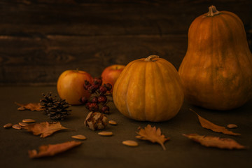 Beautiful autumn cozy still life. Pumpkins, autumn leaves, apples and cones on wooden background. Vintage decorative background with fall vegetables. Harvest time concept. Soft focus. Toned image.