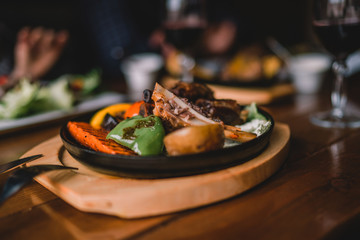 Eating and leisure concept. Dinner on the table. Tasty grilled lamb leg with vegetables and herbs on a roasting iron pan. Assorted delicious vegetables with grilled meat. Toned image. Selective focus
