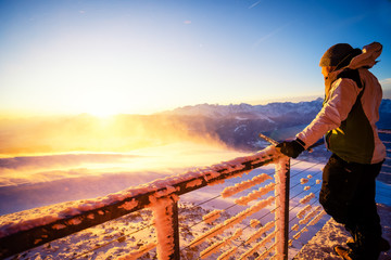 Men standing on the top of a mountain at sunrise / sunset and is looking at the sun and the mountains down the valley