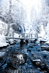 People at the Blue water in winter with snow falling, icicle in the water, trees and a big waterfall